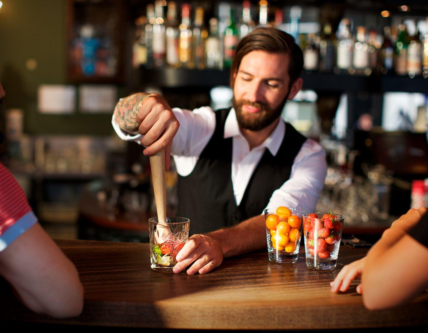 Muddling tools on a countertop, with a an orange cocktail garnished with orange and cherry.