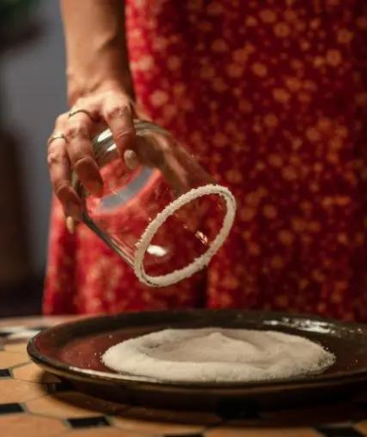 A person's hands holding a Margarita glass over a saucer of salt