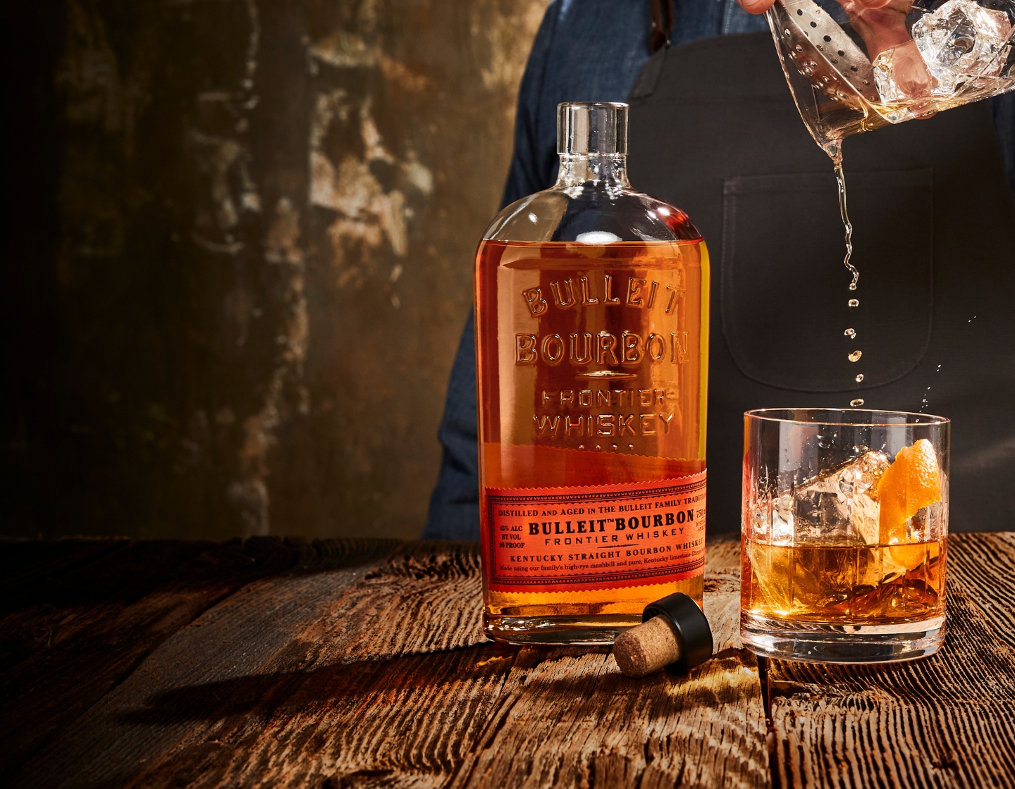 Botella de Bulleit Bourbon junto al hombre vertiendo un cóctel en un vaso
