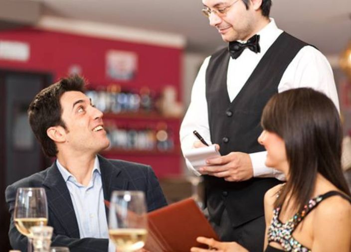 Imagem de um garçom atendendo um casal de clientes