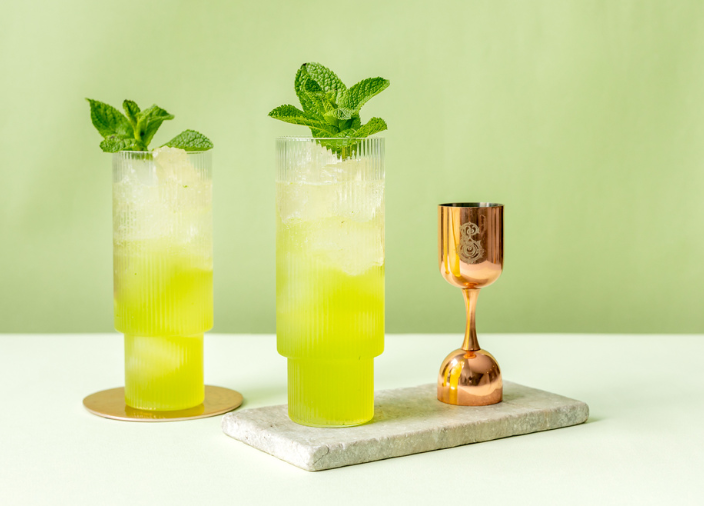 Dos cócteles CosNo, versiones sin alcohol del clásico cóctel Cosmopolitan, elaboradas con Seedlip Grove 42, junto a un medidor de alcohol de color bronce.