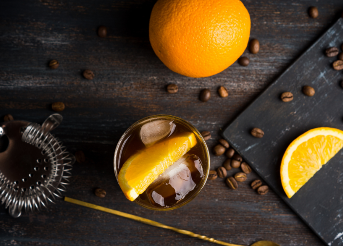 Plane view of cocktail surrounded by stirrer, coffee beans, and orange 