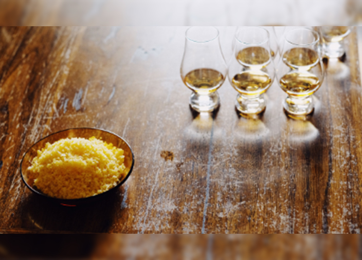 Un pequeño cuenco de madera con sal natural suave de color naranja. Una fila de pequeños vasos de whisky Glencairn en la parte de atrás.