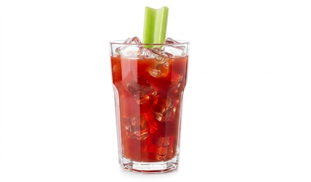 Fotografia isolada em fundo branco de um coquetel vermelho, como um Bloody Mary, servido em copo alto facetado com bastante gelo. Um talo de aipo verde fresco decora a bebida no topo.