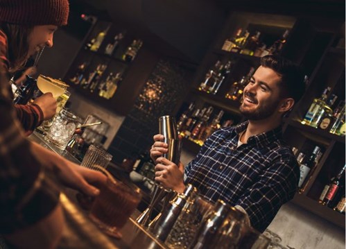 Bartender making cocktail in a shaker behind bar, smiling at guests