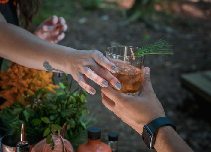 Woman_handing_tumblr_of_american_whiskey_to_man_with_plant_and_leaves_in_background
