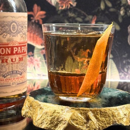 Ein altmodischer Rum-Cocktail mit einer Orangenschalen-Garnitur, der neben einer Flasche Don Papa Rum steht.