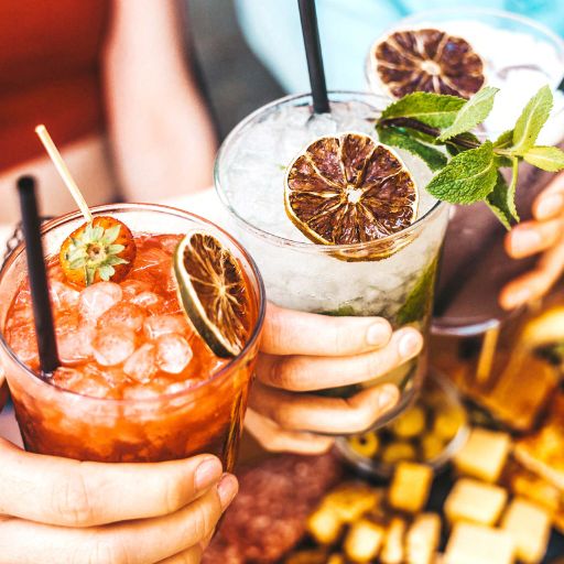 Three hands holding batched cocktails
