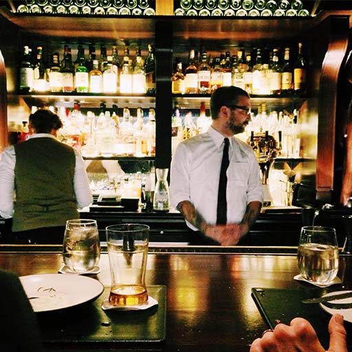 Equipe do bar trabalhando atrás de bar ocupada com clientes sentados no bar com comida e bebidas