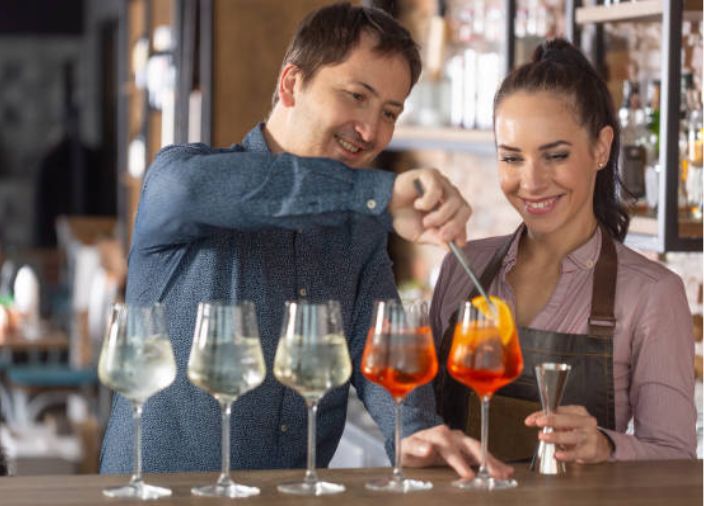 Two bartenders garnishing a selection of drinks glasses.