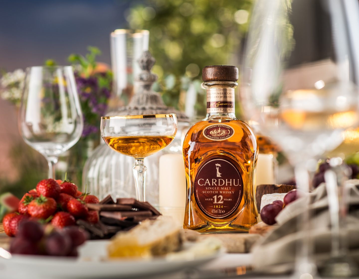 Botella del whisky single malt Cardhu sobre la mesa rodeada de platos de comida y copas de cóctel