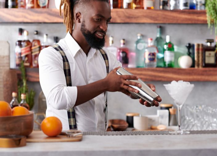 Bartender agitando uma coqueteleira com as duas mãos. 