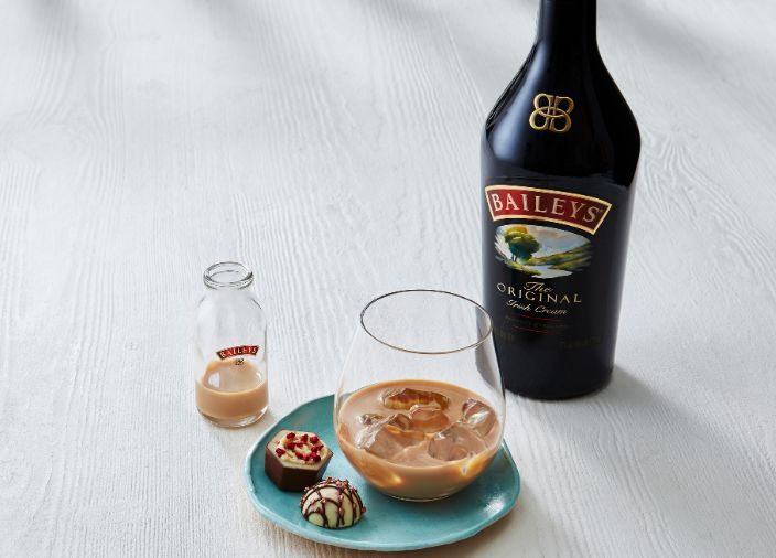 Baileys on the rocks accompanied by some chocolates sitting next to a bottle of Baileys.