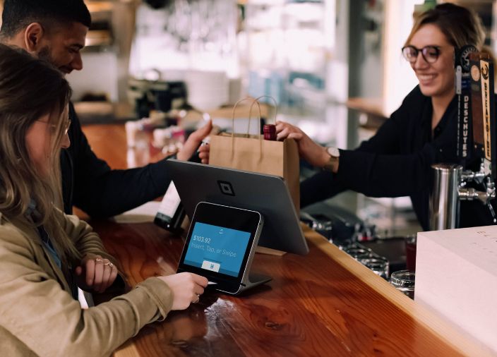  Un hombre y una mujer pagan artículos en un bar utilizando un terminal POS con pantalla.