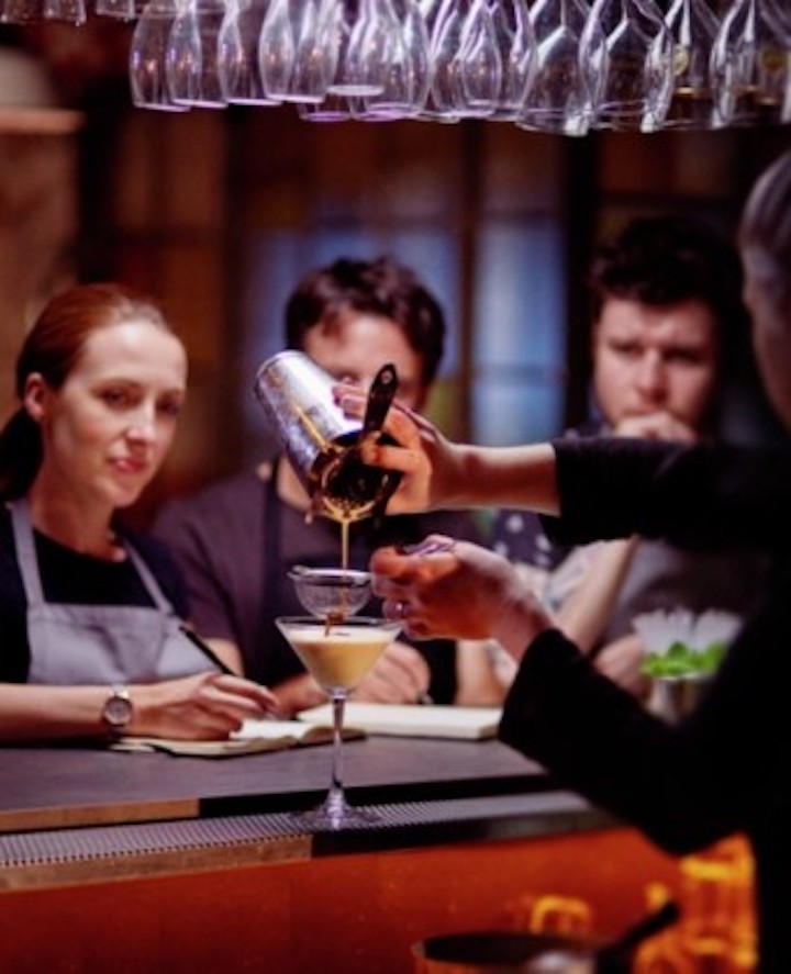 Drei Personen schauen zu, wie ein Drink gemixt wird