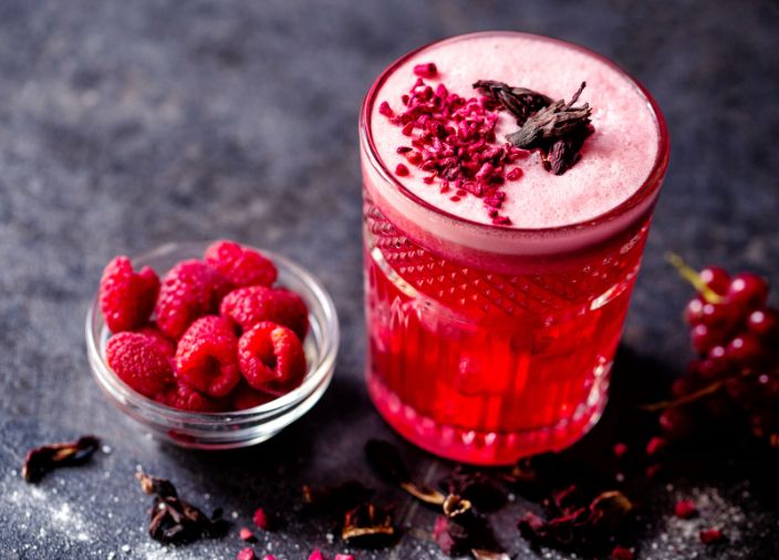 Getrocknete Himbeerstücke als Garnierung eines Cocktails mit roten Beeren, serviert in einem kurzen Becherglas.