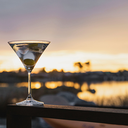  A Dirty Martini, with olives in the glass against a sunset background.