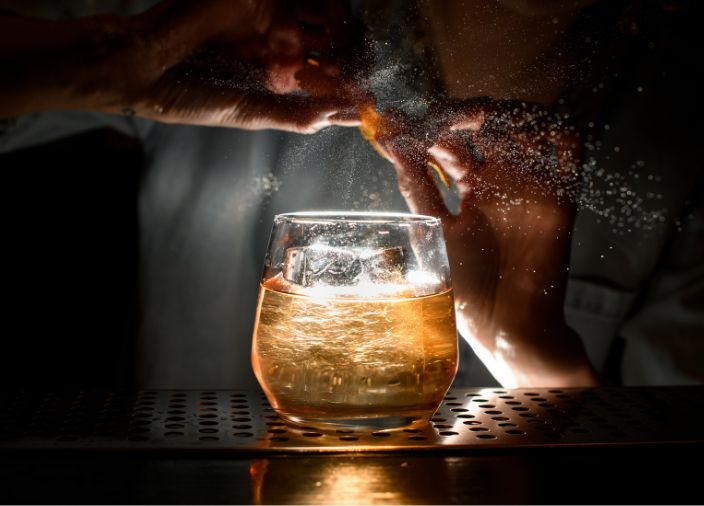 Um copo de American Whisky com gelo e o bartender borrifando laranja no copo