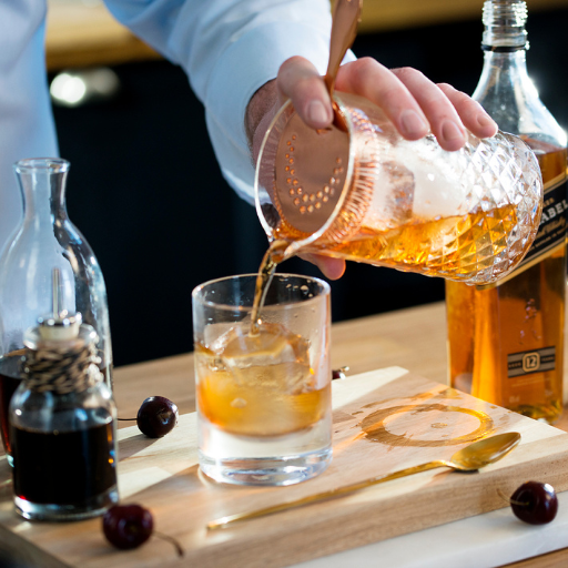 Whiskey cocktail being poured from shaker into glass with ice 