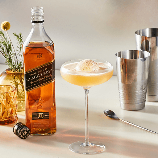 Botella de Johnnie walker black label junto a cóctel con guarnición y coctelera