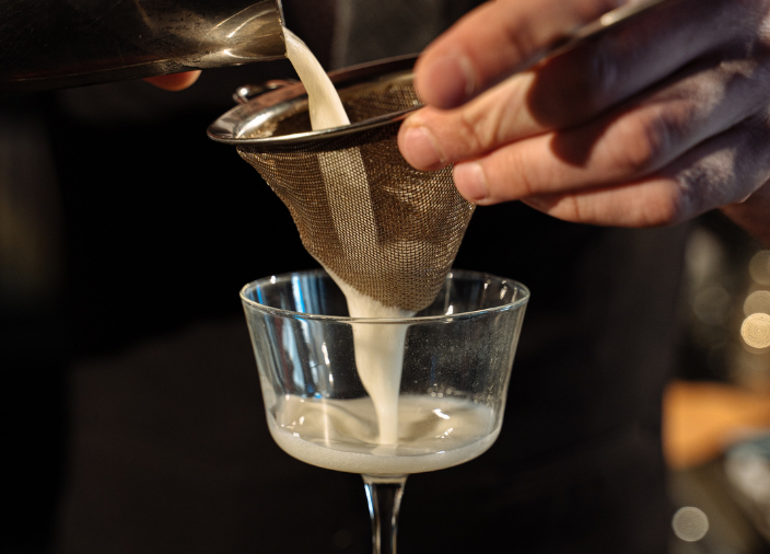 Eine Hand gießt einen Cocktail durch ein Sieb.