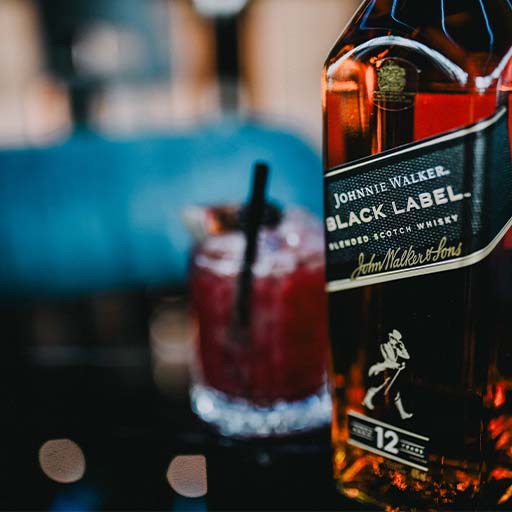Close shot of a bottle of Johnnie Walker Black Label with a red/pink cocktail in the background