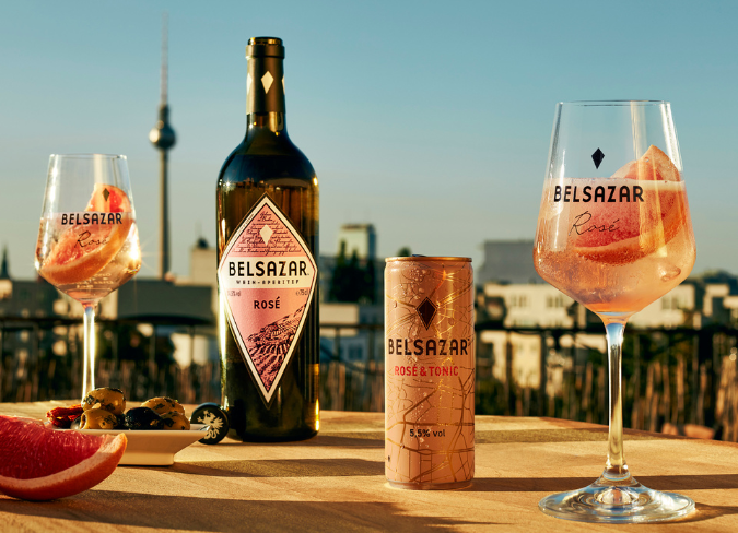 Botella de Belsazar rosado en una mesa al aire libre al atardecer junto a dos copas de vino llenas de bebidas rosadas