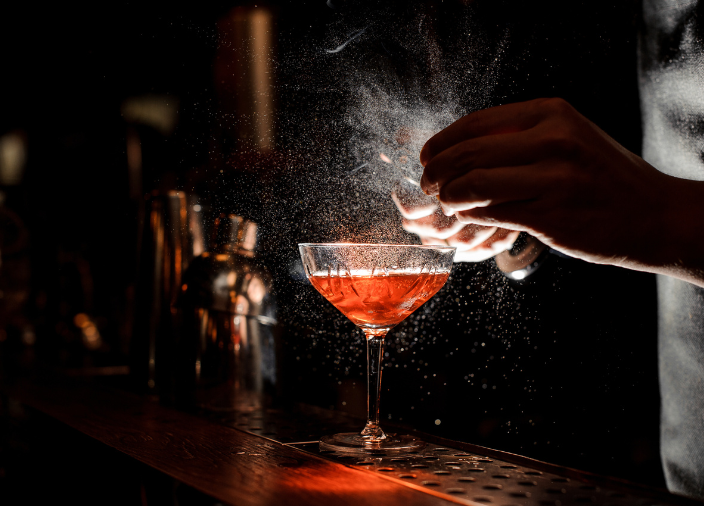 El bartender rociando jugo de naranja sobre el martini.