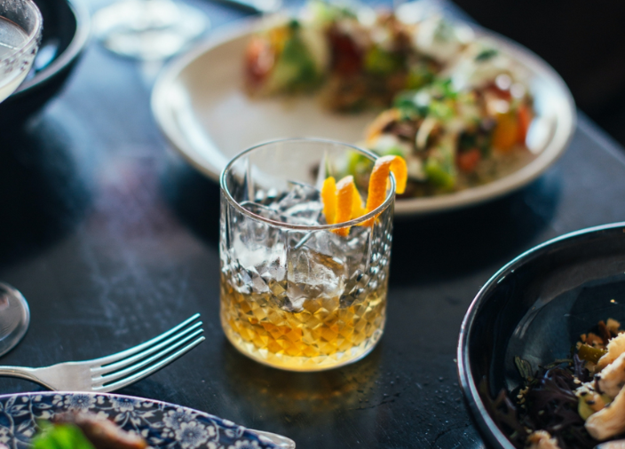 Copo cheio de whisky com pratos de comida ao fundo