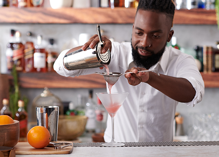 Bartender with a cocktail shaker interscting with customers sitting at the bar.