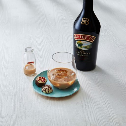 Baileys on the rocks accompanied by some chocolates sitting next to a bottle of Baileys.