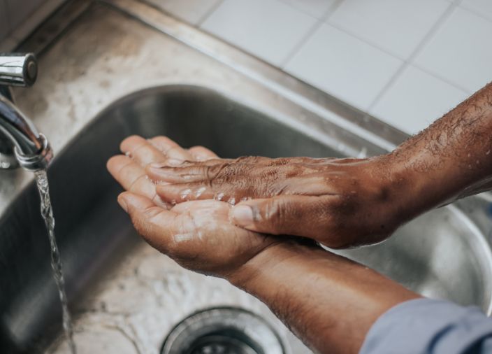 Hands being washed in a stainless steel sink.