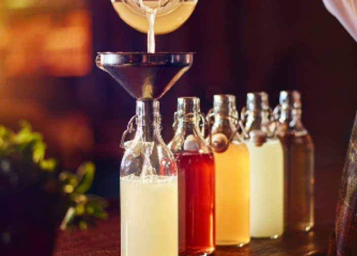 Glass of Juice with metal straw beside large glass bottle of juice and plate of oranges