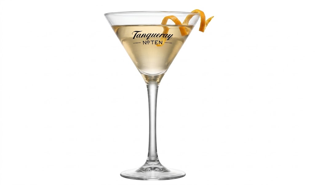 Coquetel claro em uma taça de martini de haste longa, com o logotipo "Tanqueray No TEN" impresso em preto no vidro. A bebida é decorada com um fino twist em espiral de casca de laranja apoiado na borda direita. Fundo branco.