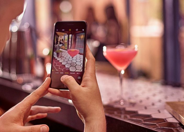 Person taking photo of cocktail at bar