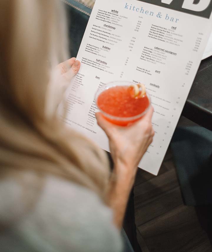 A guest reading the food menu with a cocktail in hand