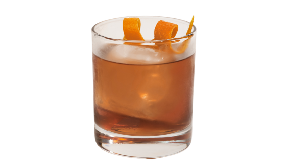 Coquetel de cor âmbar em copo baixo com uma grande pedra de gelo central. Uma casca de laranja em espiral decora o topo da bebida. O copo, levemente suado de condensação, projeta uma sombra à esquerda sobre um fundo totalmente branco.
