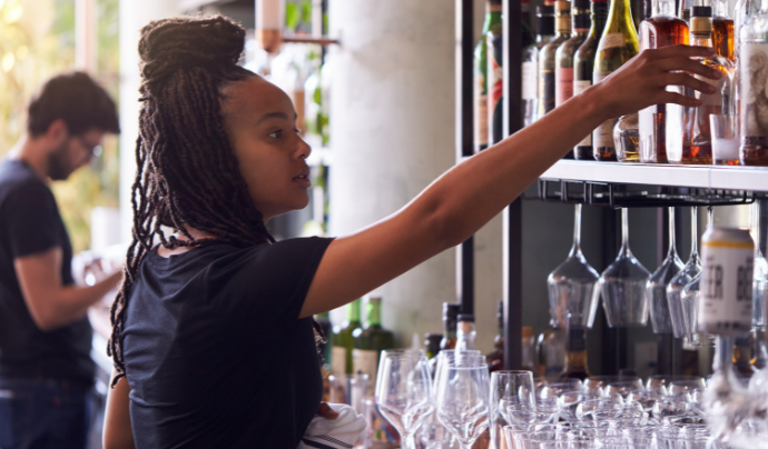 Bartender do sexo feminino posicionando estoque na parte de trás do bar.