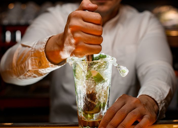 Barkeeper muddelt Limettenschalen in einem Glas