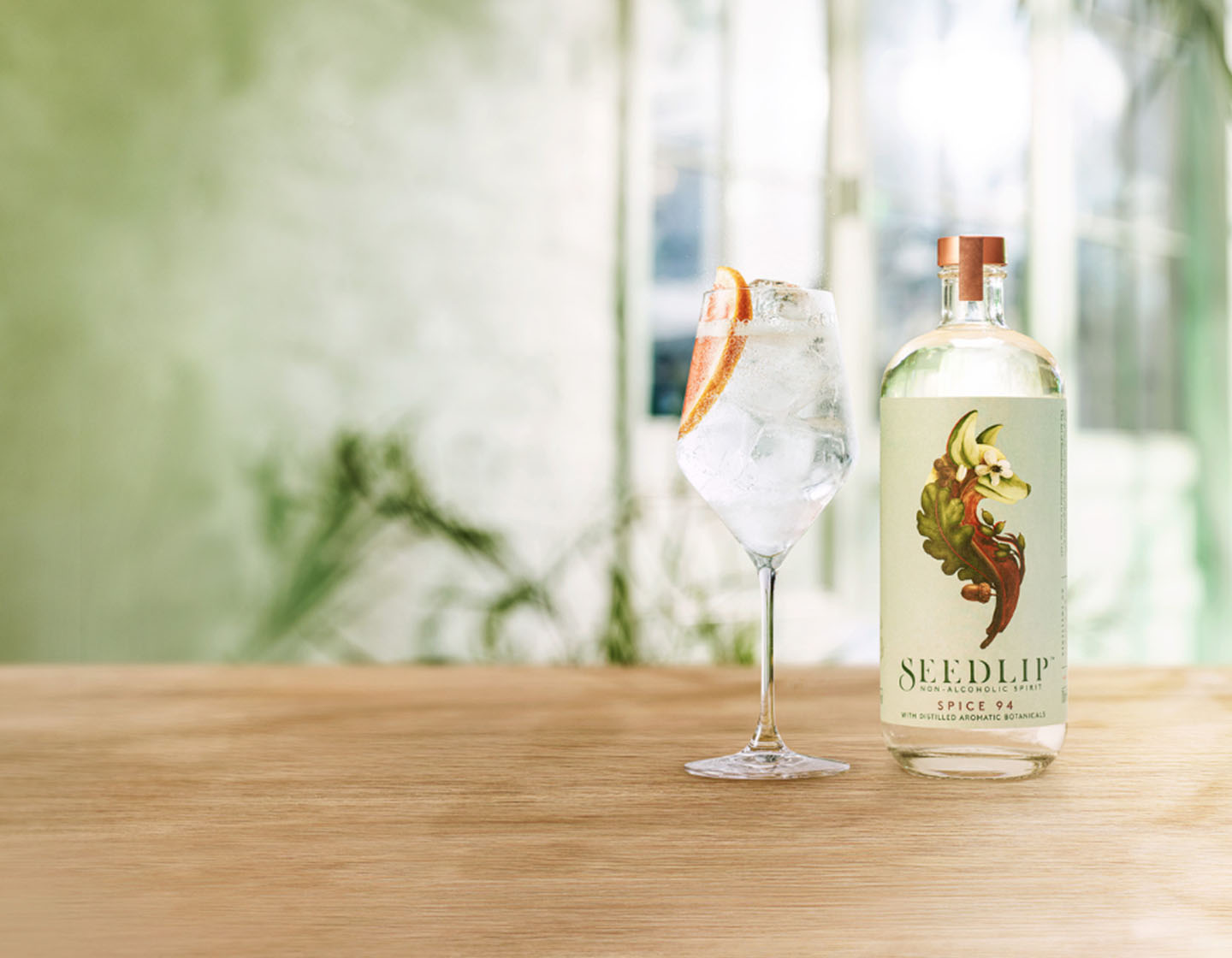 Bottle of Seedlip Spice 94 on table beside cocktail