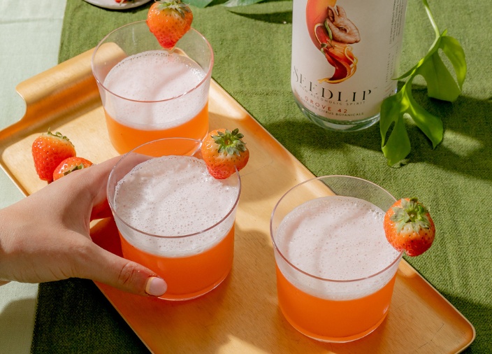Três coquetéis coloridos cercados por três garrafas diferentes de destilados não alcoólicos da Seedlip