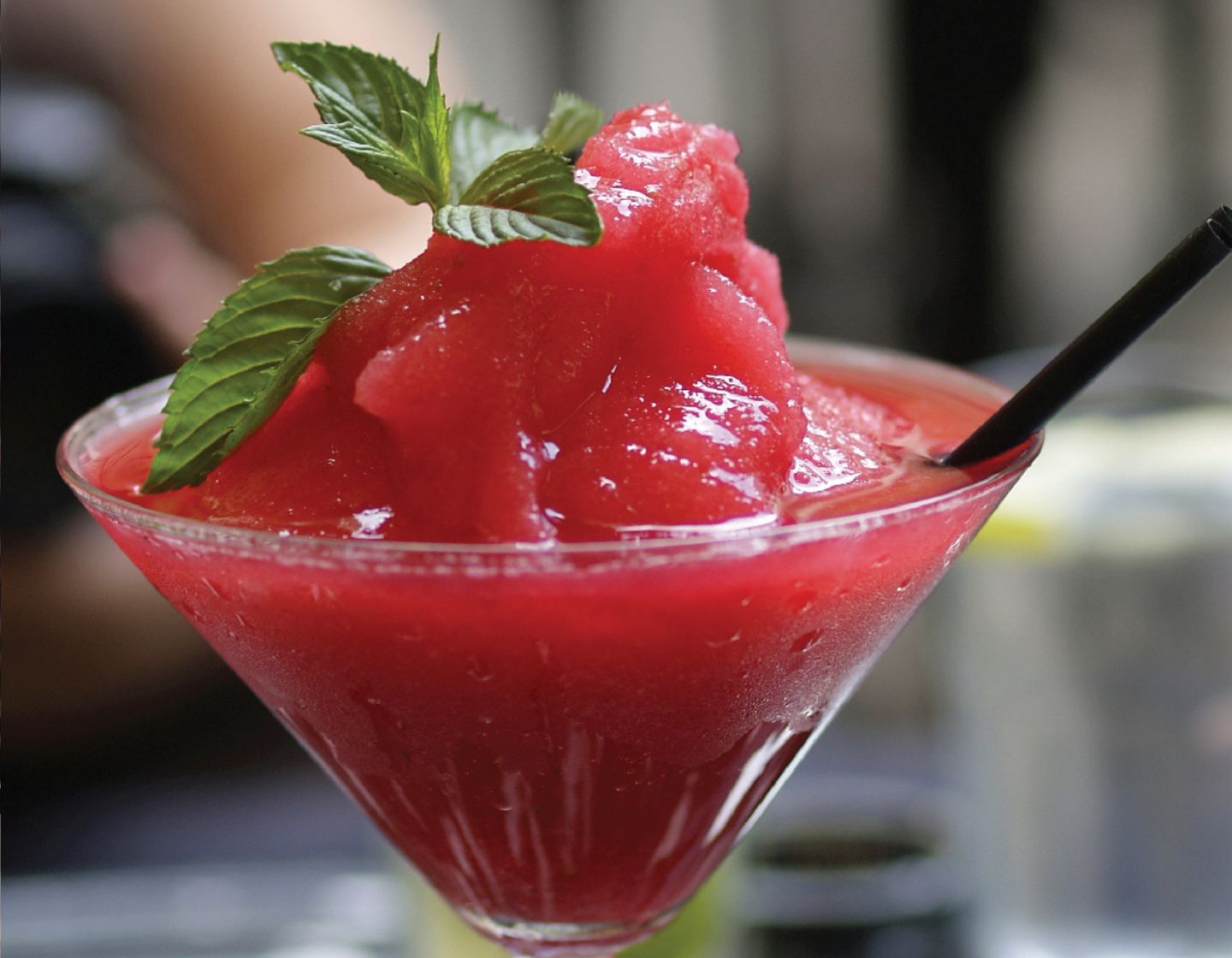 Bright red strawberry daquari in a cocktail glass garnished with mint leaves.