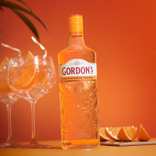  Bottle of Gordon’s Mediterranean gin beside two G&T glasses against orange background 