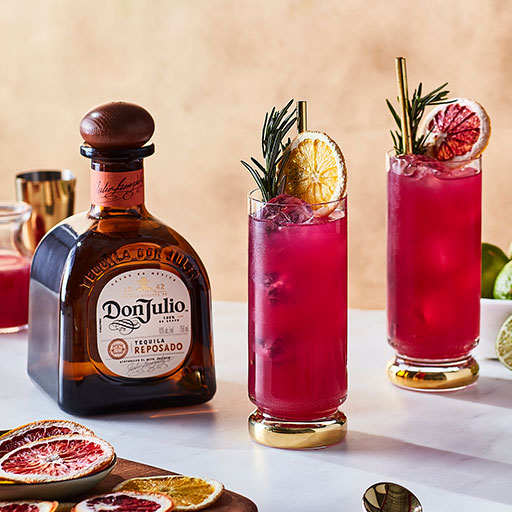Bottle of Don Julio Reposado tequila in front of tray of two orange cocktails 