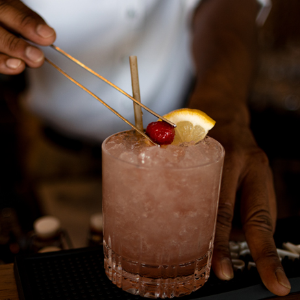 Cherry being placed on the top of a frozen cocktail garnished with lemon.
