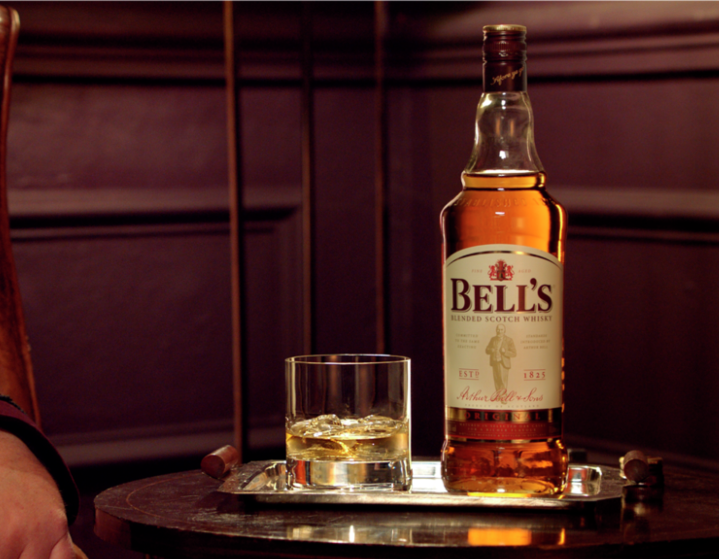Botella de whisky Bell's en una bandeja junto a un vaso lleno de whisky