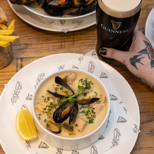 Hand holding a pint of Guinness next to a bowl of clam soup