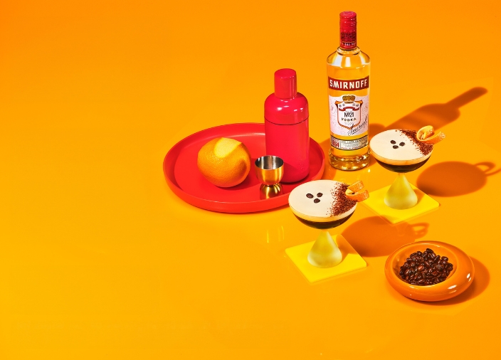 A bottle of Smirnoff No.21 with two Espresso Martinis and ingredients on an orange background