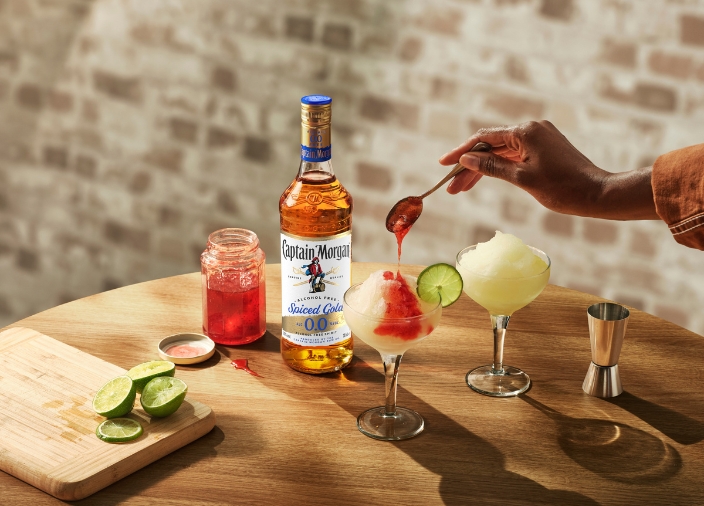 Eine Flasche Captain Morgan Spiced Gold 0.0% alkoholfrei steht neben zwei Cocktails, die gerade garniert werden