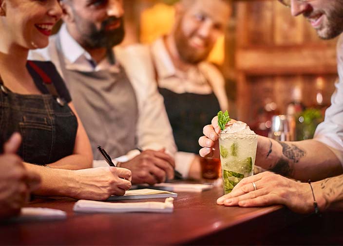 Eine Gruppe Barpersonal beobachtet die Zubereitung eines Cocktails.